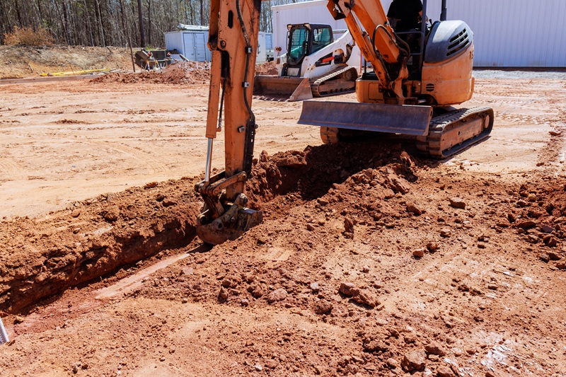 Heavy machinery is digs trench as workers prepare for construction location.